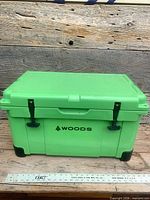 Front view of green Woods cooler showing logo, dual T latches, overall size reference with ruler