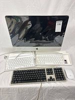 Front view of iMac with three keyboards, Magic Mouse and power cable
