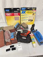 All items in lot laid out: two sanders, dust bag, sandpapers, sanding belts, blocks, filler