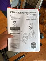 User manual titled HealthRider H30x User's Manual held in front of bike