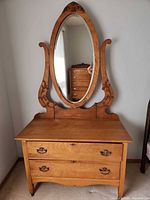 Front view of dresser showing two drawers, brass pulls and attached oval mirror with carved supports