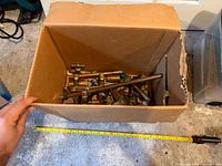 Full view of cardboard box with assorted plumbing parts and tape measure for scale
