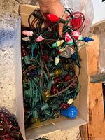 Box containing tangled green-wire C7 light strings with coloured teardrop and novelty figure bulbs
