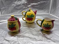Front view of teapot, sugar bowl with lid, and creamer showing fruit motif and colors