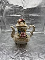 Full view of ivory porcelain teapot with lid showing applied multicolor flowers and three footed base