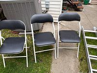 Three folding chairs with white frames and black padded seats