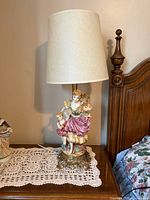 Full view of porcelain figurine lamp with shade on bedside table