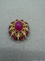 Front view showing central oval red cabochon, surrounding smaller cabochons and white accents