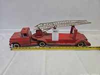 Full left-side view of red Buddy L fire truck with ladder retracted, tape measure shows length