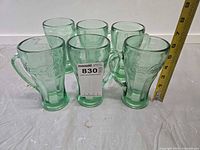 Front view of six green Coca-Cola mugs with measuring tape indicating 6 inches