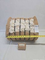 Front view of cotton bale showing burlap wrap, metal bands, cotton fiber, attached paper tag and ruler for scale; miniature bale placed in front