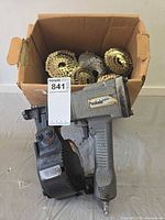 Paslode nailer in front of box containing multiple coils of nails