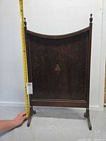 Front view showing arched top, finials, beaded trim, diamond inlay, measuring tape indicating height