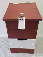 Front view of red and white wood bin with hinged top and lower drawer