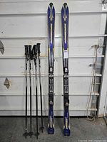 Pair Rossignol skis and four ski poles leaning against wall