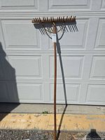 Full view of wooden garden rake leaning against garage door