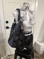 Front of large black faux leather tote on mannequin showing vertical side zipper and shoulder straps