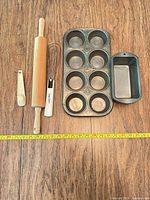 Group shot of muffin pan, single loaf pan, rolling pin, whisk, scoop with tape measure for scale