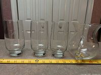 three tumblers and pitcher lined by ruler showing scale