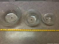 Three clear glass swirl ribbed bowls with measuring tape for scale