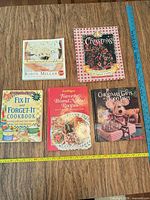 Front covers of all five cookbooks laid out with measuring tape