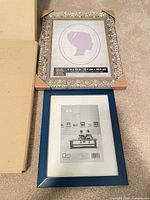 Two picture frames, silver Studio Décor metal 9x12 and blue Furio wood 8x10, on carpet