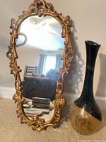 Front view of ornate gold framed mirror beside tall amber glass vase