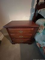Front view of one bedside table showing three drawers and brass-tone handles