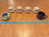 All six mugs lined beside yardstick showing scale