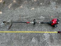 Full view of Troy-Bilt gas string trimmer laid out next to tape measure showing ~60 in length