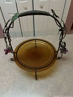 Front view showing amber glass plate seated in metal stand with handle and grape clusters