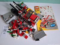 Loose LEGO pieces, partially built red vehicle, instruction manual visible