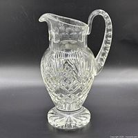 Side view of clear lead crystal pitcher showing diamond and starburst cuts, handle, and pedestal base