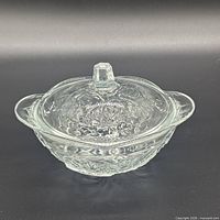 Side view of clear pressed glass covered bowl showing floral pattern and handles