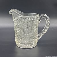 Side profile of clear pressed glass pitcher showing hobnail texture, starburst panel and spout
