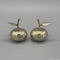 Front view of both brass apple shakers showing shape and leaf detail
