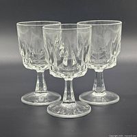 Front view of three matching clear faceted wine glasses standing together