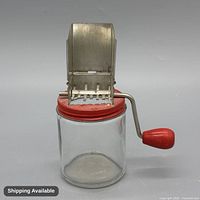Front view of glass jar nut grinder showing red lid, metal grater and crank handle