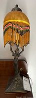 Full view lamp showing domed shade, beaded fringe, figural base