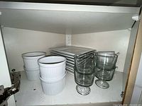 cabinet shelf holding ramekins, square plates, glass bowls