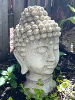Front angled view of concrete Buddha head statue showing full shape and surface texture