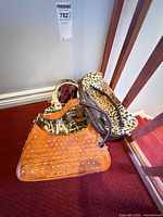 Three handbags stacked: orange studded, leopard print, printed canvas