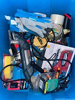 Overview of blue bin containing Bosch saw, Weed Eater spool, Master Lock padlock, gloves, tape, pliers, sponge, stapler, electrical tape and assorted accessories