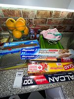 Consumable wrap rolls, grater front, glass bowl with fruit, shortbread tin, towels and colander all on counter