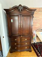 Full front view of dark brown ornate armoire showing cabinet doors and drawers