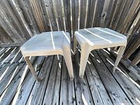 Both beige plastic outdoor side tables shown side by side on deck