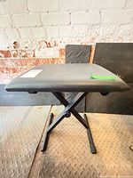 Overall view of black adjustable keyboard bench showing seat, X-frame, adjustment knob and rubber feet