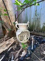 Full view of resin urn beside fence showing relief scene and handles