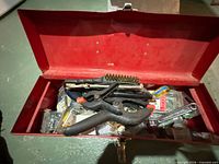 Open red toolbox showing wire brush, pliers, wrench and hardware packs