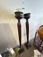 pair of tall dark brown wooden candle holders with glass jar candle on left unit
